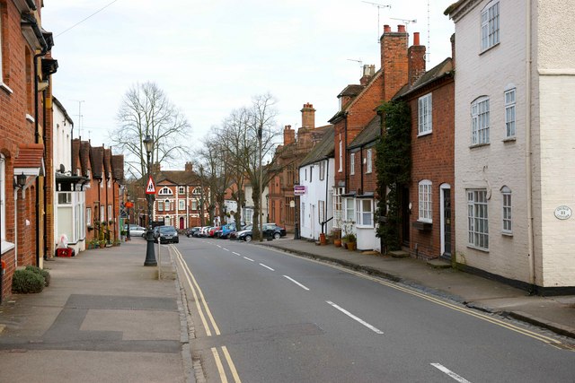 Quiet residential street lined with brick houses, parked cars, and leafless trees on a sunny day.